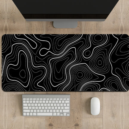 Black and white topographic desk mat on a wooden desk with a computer monitor, keyboard, and mouse.