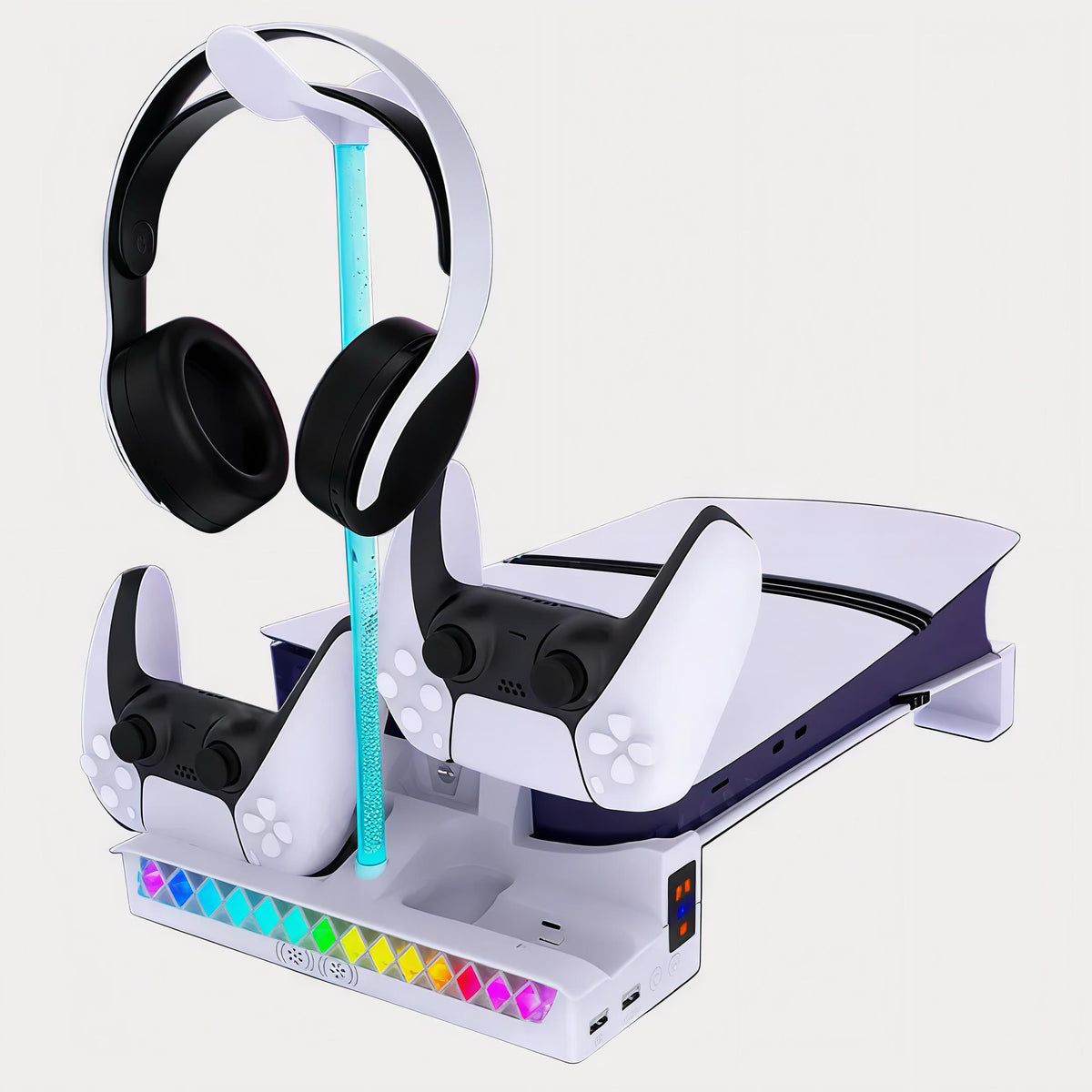 A white and black PlayStation 5 console shown with two matching controllers, a pair of over-ear headphones on a stand, and a turquoise charging cable, all arranged on a white charging dock with colorful LED accents against a light gray background.