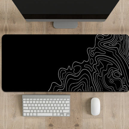 Black desk mat with white line art design on a wooden desk with a computer monitor, keyboard, and mouse.