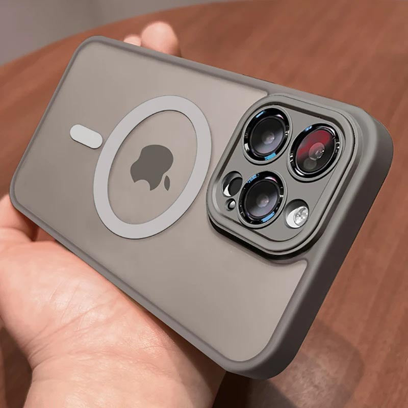 A titanium gray protective phone case with a MagSafe ring and camera cutout, held in a hand over a wooden surface.