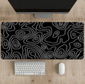 Black and white patterned mouse pad on a wooden desk with a computer monitor, keyboard, and mouse.