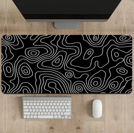 Black and white patterned mouse pad on a wooden desk with a computer monitor, keyboard, and mouse.