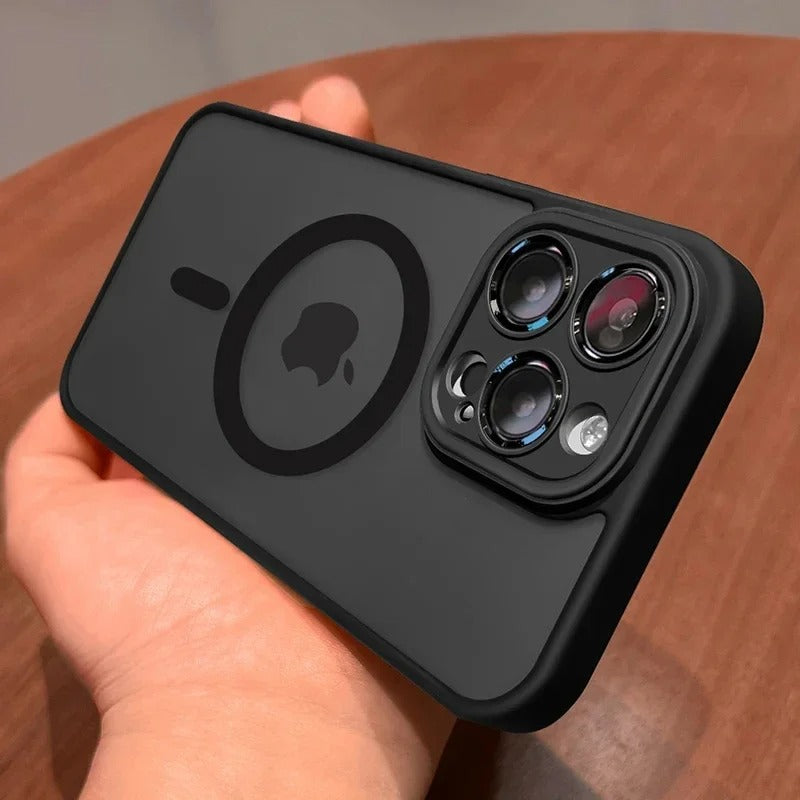 A black protective phone case with a MagSafe ring and camera cutout, held in a hand over a wooden surface.