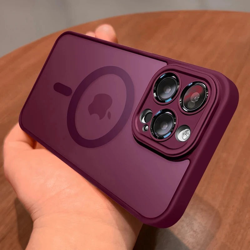A plum red protective phone case with a MagSafe ring and camera cutout, held in a hand over a wooden surface.