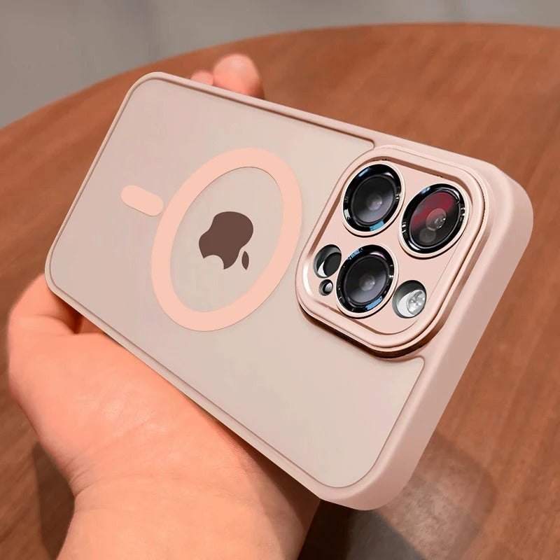A light pink protective phone case with a MagSafe ring and camera cutout, held in a hand over a wooden surface.